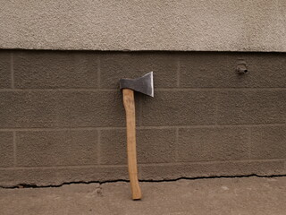 Axe with wooden handle leaning against concrete wall. Rustic rural tool, simplicity, worn metal...