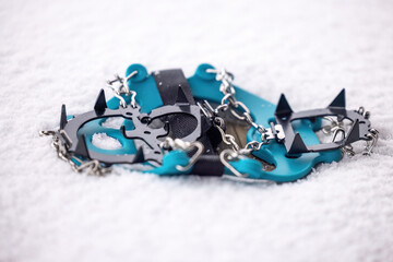 Blue ice cleats with metal spikes lying on fresh snow, winter traction gear for hiking with clean background
