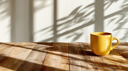 A vibrant yellow mug sits on a rustic wooden table, casting artistic shadows against the white wall, offering a cozy and inviting feel to the serene setting.