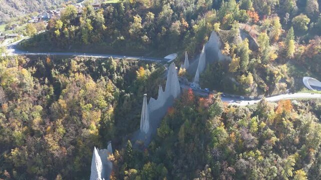 Aerial view of the striking Pyramides d'Euseigne, piercing the landscape amidst a tapestry of autumnal trees and winding roads, Heremence, Valais, Switzerland.