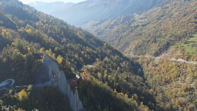 Aerial view of the majestic Pyramides d'Euseigne standing tall amidst the colorful autumn foliage and winding roads of the Swiss Alps, Heremence, Valais, Switzerland.