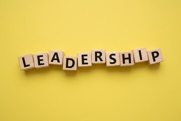 Wooden blocks spelling LEADERSHIP, loosely arranged, bright yellow background, minimal leadership concept