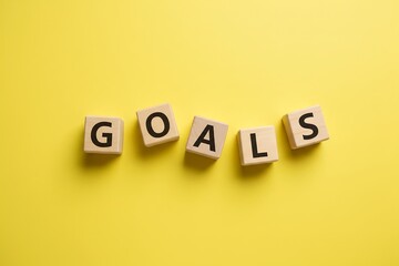 Wooden letter cubes spelling GOALS, not perfectly aligned,  bright yellow background, flat-lay self-improvement concept