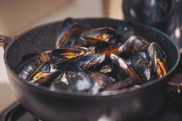 A pot filled with fresh mussels sits on a stove. Steam rises from the pot as the mussels cook. The kitchen is bright and the focus is on the preparation of the seafood dish