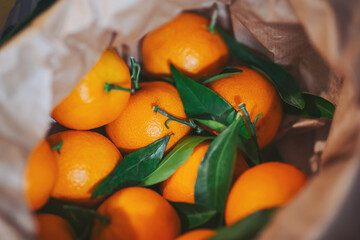 Fresh oranges are arranged with green leaves inside a brown paper bag. The setting looks like a kitchen, and the oranges are bright with a healthy appearance, ready for use