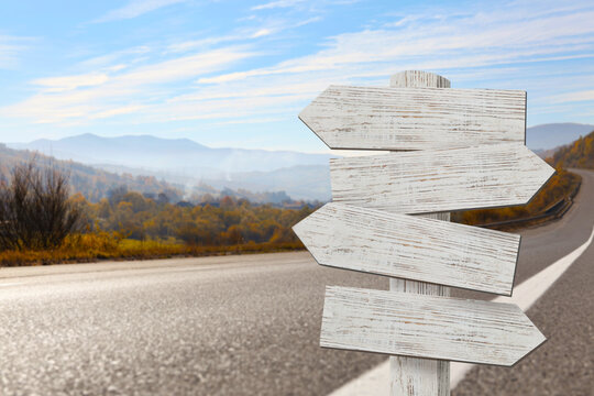 Wooden signpost with arrows pointing in different directions on road
