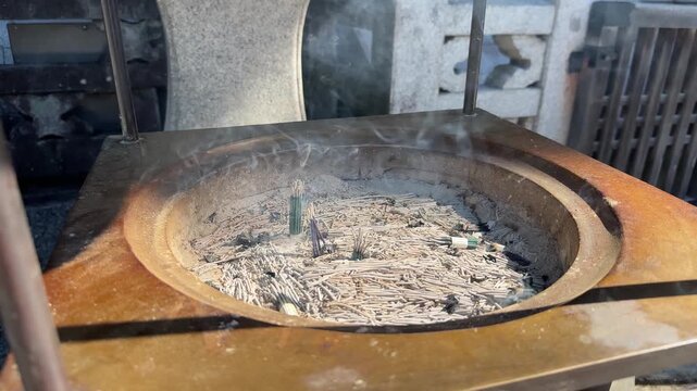 Smoke rising from burning incense sticks in a traditional Japanese censer at a Buddhist temple