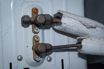 Close-up detail of copper pipe connections on an air conditioning (AC) unit with worn valves and pipe insulation.
