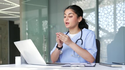 Confident female doctor talking on video call using laptop in hospital clinic. Smiling woman medical worker physician is having remote consultation with patient sitting at desk at workplace in office