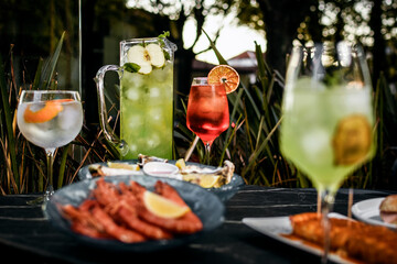 Mixed cocktail drinks and sangria with snacks on restaurant table outdoors at sunset