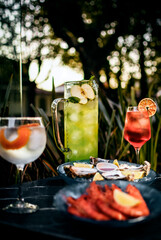 Mixed cocktail drinks and sangria with snacks on restaurant table outdoors at sunset