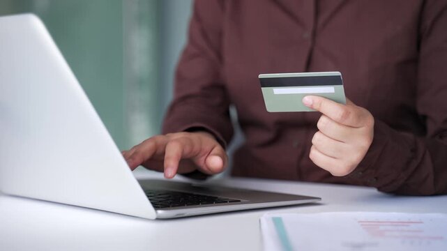 Close up of female hands typing on laptop to make online transaction with credit card at desk in business office. Businesswoman shopper makes digital payment, e-commerce, e-shopping.