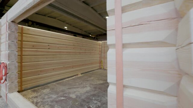Partially assembled wooden cabin structure inside a workshop, with numbered timber logs, window cutouts, tools, and straps visible. Interior space offers copy space