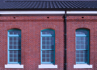 Fototapeta premium Red Brick Building Facade with Three Turquoise Windows For branding,calendar,postcard,screensaver,wallpaper,poster,banner,cover,website.High quality photo