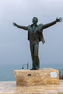 bronze statue of singer domenico modugno (mister volare) with open arms, gazing at the adriatic sea in polignano a mare, apulia, italy, under an overcast sky