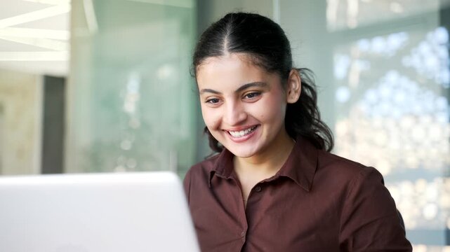 Satisfied happy businesswoman reading good news on laptop sitting at workplace in business office. Smiling glad female employee celebrates success, rejoices at positive message on computer. Close up