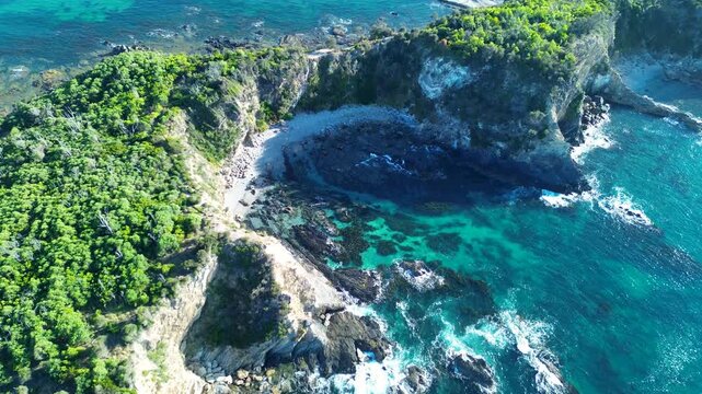 Drone aerial landscape of Orangestone Cove framed by cliff face bushland with natural ocean reef sandy beach inlet and rocky headland along Malua Bay coastline South Coast Australia travel nature