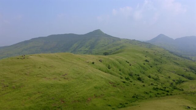 Aerial dolly in across rolling grassy hills and distant peaks under blue sky in Sanjay Gandhi National Park