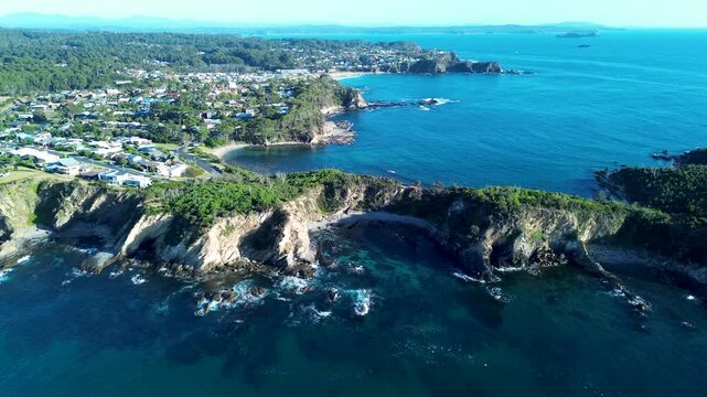 Drone aerial landscape of rocky ocean headland with a reef beach cove surrounded by suburban town homes and rural bushland forest coastline in Malua Bay South Coast Australia travel tourism holidays
