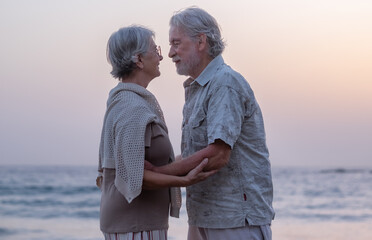 Cuddles for an elderly couple embracing while standing on a rocky beach at sunset, expressing love and affection. Retirement lifestyle, vacation, freedom.