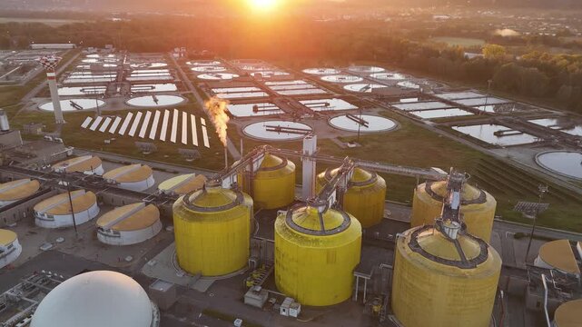 Aerial view of the wastewater treatment plant featuring yellow tanks and circular pools, under a vibrant sunrise, Turin, Piemonte, Italy.