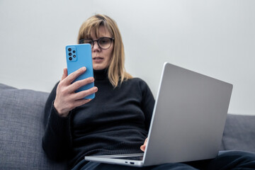 Woman holding a phone next to laptop. Concept of multitasking, connection and modern digital lifestyle. It suggests the integration of mobile technology and personal computing in everyday productivity