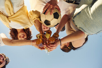 View from below of people that are cheering with beer bottles