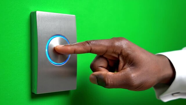 Close-up of a hand pressing a glowing blue button on a metal panel against a green background