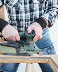 Craftsman. Adult carpenter using an electric sander to smooth an old wooden window. Construction industry, carpentry, housework do it yourself. Restoration.