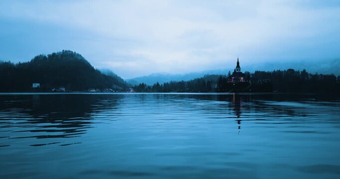 Mari&auml; Himmelfahrt Kirche auf der Insel im Bleder See w&auml;hrend der blauen Stunde, ruhige Wasserfl&auml;che mit dezenter Bewegung und Spiegelung, beleuchtete Kirche bei D&auml;mmerung in Slowenien