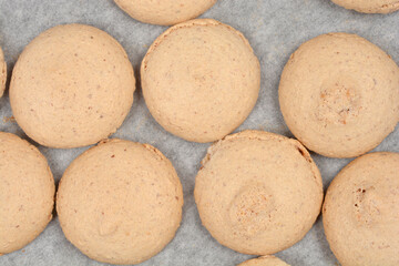 Fototapeta premium A high angle full frame shot of many baked golden beige french macaroon shells cooling on white parchment paper after being removed from the oven