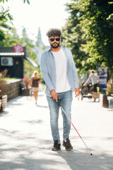 Wearing casual clothes, having a walk. Blind man with white cane and sunglasses is in the city