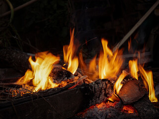 Burning wood logs in bonfire with hot orange flames and sparks at night.