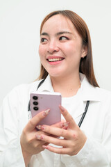 Portrait of young Asian female doctor against white background using phone smiling and thinking
