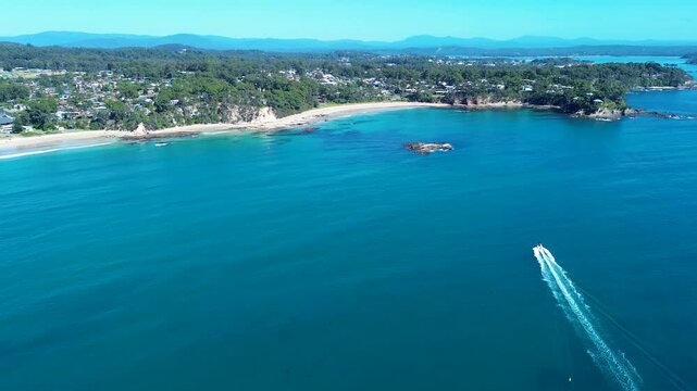 Drone aerial landscape of fishing boat arriving in ocean cove inlet with rocky coastline reef and town suburban housing in background at Denhams Beach in Batemans Bay Australia travel nature holidays