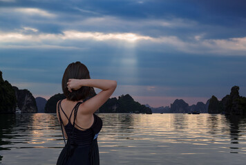 Fototapeta premium A beautiful young asian girl stands at the front of the ship and watches the evening sunset - Sunset In The Morning On The harbour In Ha long Bay In Vietnam