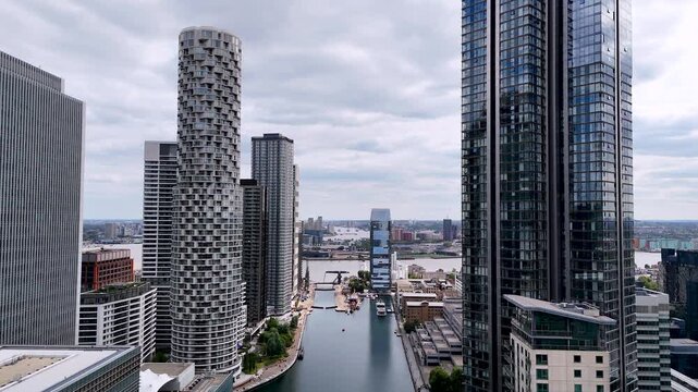 Aerial tracking shot over the docks of Canary Wharf, London. Drone flies forward and backward along the river between modern skyscrapers, showcasing the financial district, waterfront and contemporary