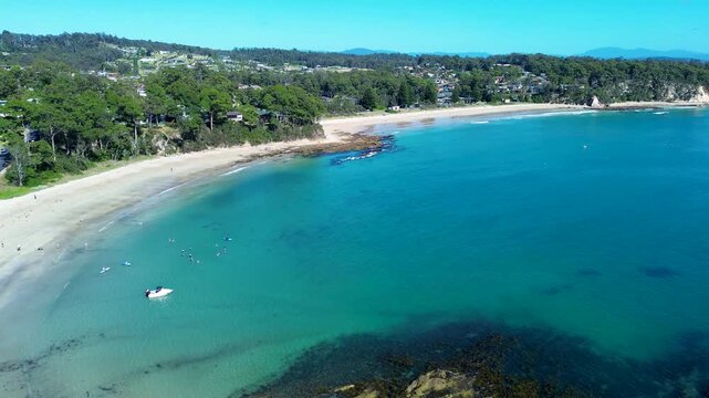 Drone aerial landscape showing boat docked on ocean sandbar with community swimmers at Wimbie Beach cove and neighbourhood town suburbs in background Batemans Bay Australia travel tourism and holidays