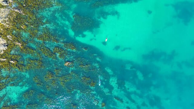 Drone aerial landscape of kayaker and paddle board rider cruising on water surface through ocean reef channel inlet with rocky seaweed boulders in Batemans Bay Australia tourism leisure nature travel