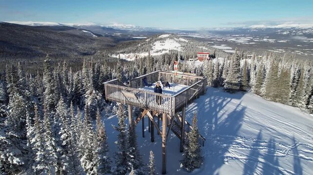 Pulls out from Charles Huang on an observation deck to reveal the vast, snow-covered landscape and nearby mountains near Mount Sima, Yukon