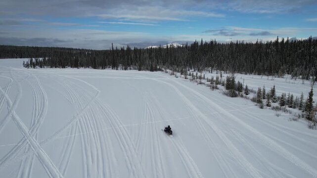 Tourists rides a snowmobile across vast, snow-covered Murray Lake with tracks visible in the snow, near Mount Sima and Whitehorse, Yukon