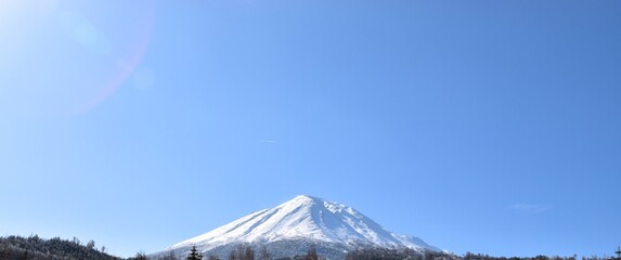 A majestic view of the snow-capped peak of Mount Bandai in Fukushima Prefecture, Japan, standing tall against a vast, clear blue sky on a sunny day, representing the beauty of Tohoku nature.