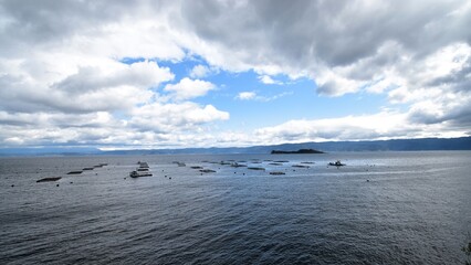 A scenic view of aquaculture rafts floating on the calm waters of Wakasa Bay in Fukui Prefecture, Japan, under a dynamic cloudy sky, showcasing the coastal fishery landscape of the region.