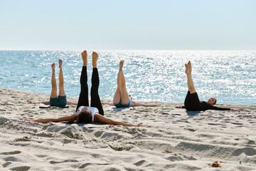 Group yoga session practicing leg raises on Baltic Sea sandy beach in bright daylight