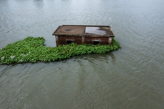 Aerial view of a lonely building overtaken by lush green vegetation amidst the murky water, Aminbazar, Dhaka Division, Bangladesh.
