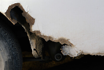 Severe rust damage and corrosion on white car fender.