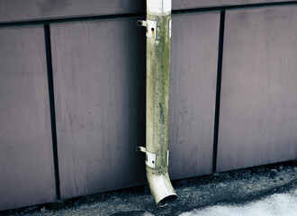 Old mossy metal gutter pipe on modern industrial wall.