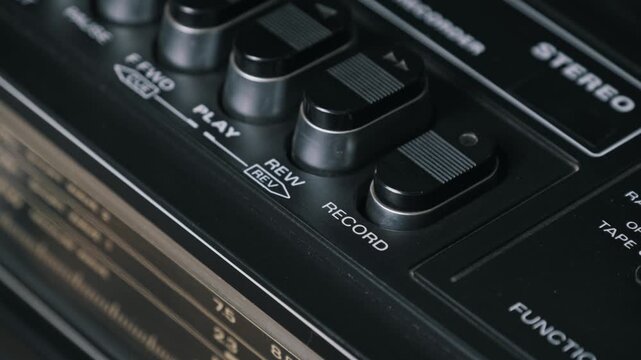 Macro close-up of a finger pressing the black record button on a vintage cassette player. The silver trim details and playback controls highlight the retro 80s design.