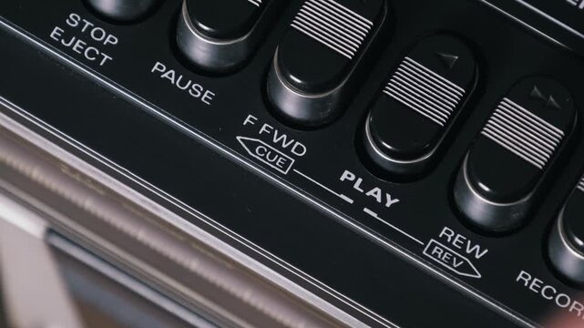 Detailed side angle of a finger pushing play then stop on a vintage cassette player. The black ridged buttons and chrome accents highlight the retro audio design.