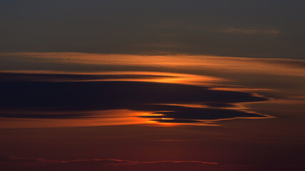 A dramatic low-light landscape featuring horizontal layers of dark clouds pierced by intense orange and red sunset light. 